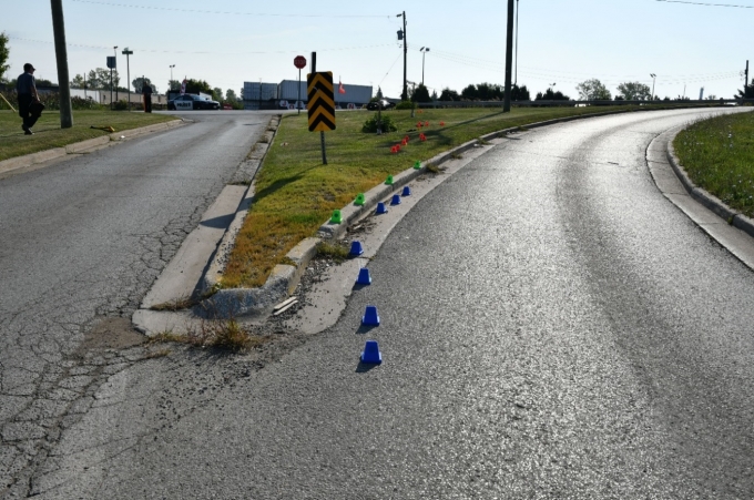 Figure 2 - This photograph was taken by SIU FI and faces east on Campbell Street where the southbound ramp to Indian Road South commences. The blue cones depict the tire mark made by the front tire and the green cones depict the tire mark made by the rear tire of the Kawasaki motorcycle. The orange cones depict the gouges in the grass. The red circle depicts the resting location of the Kawasaki motorcycle.